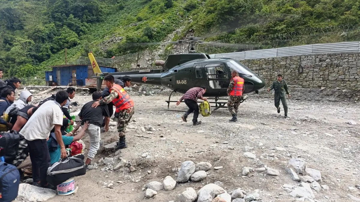 Villagers with bags carried toward a Nepali Army helicopter on a stony riverbank during the flood rescue