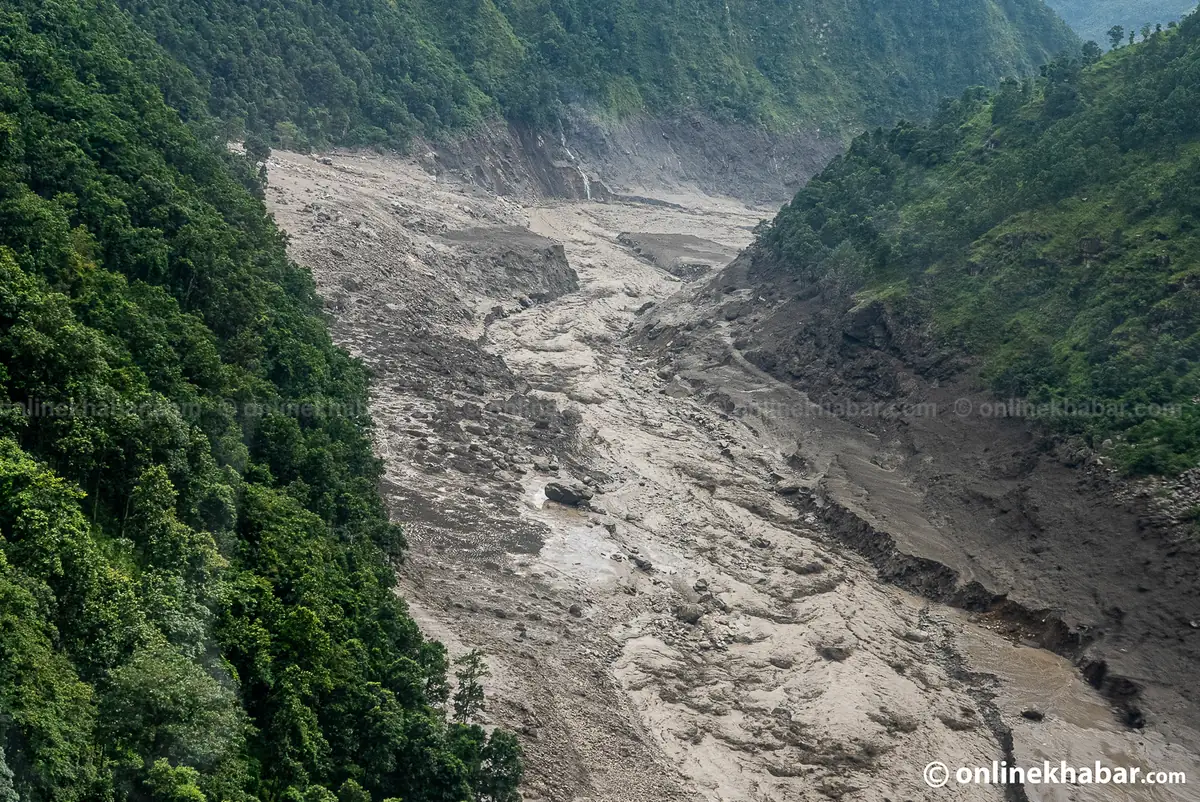 Aerial view of an entire valley floor filled bank to bank with grey flood debris between green hillsides