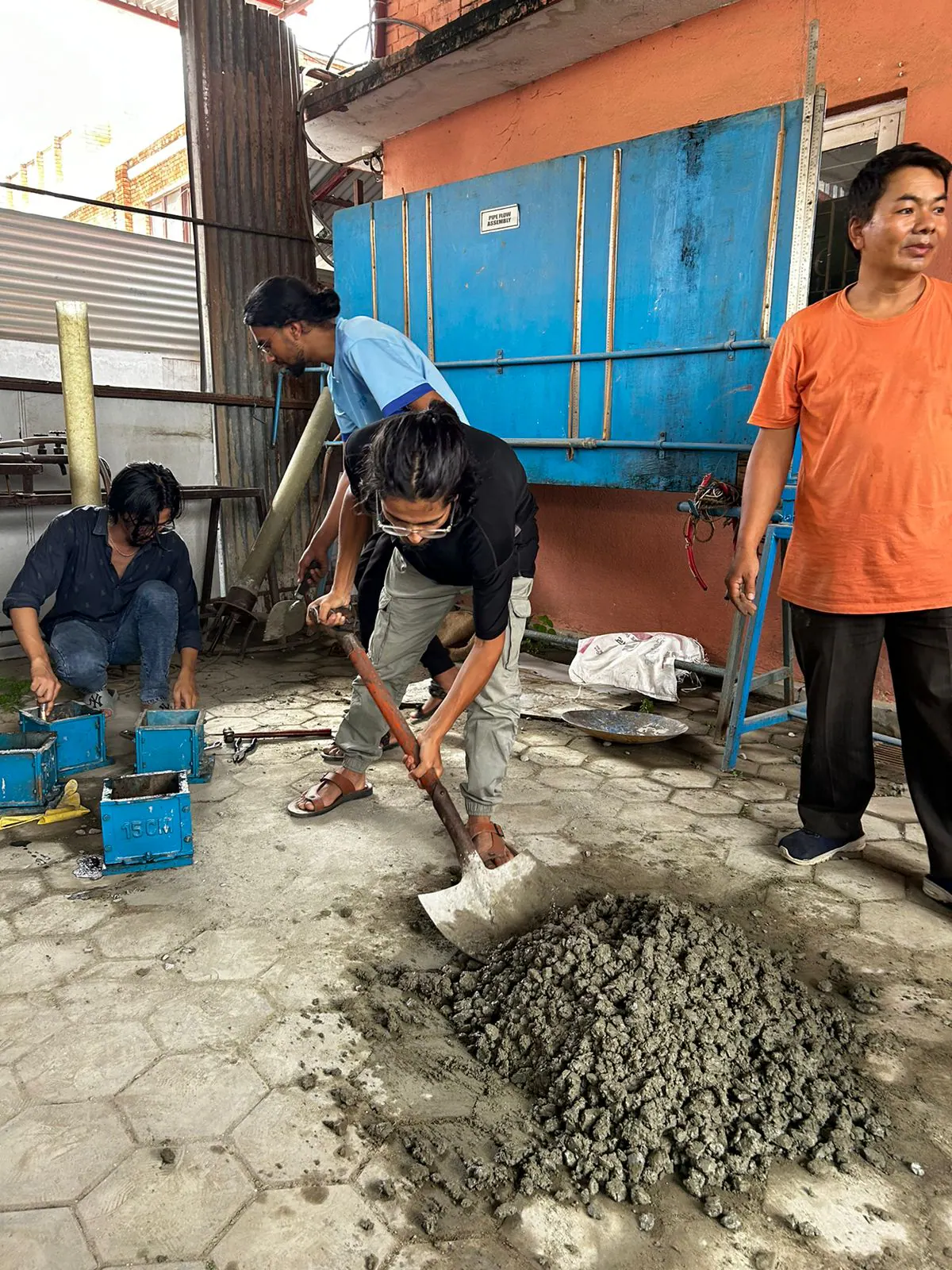 Students mixing mortar on the ground while an instructor watches the work